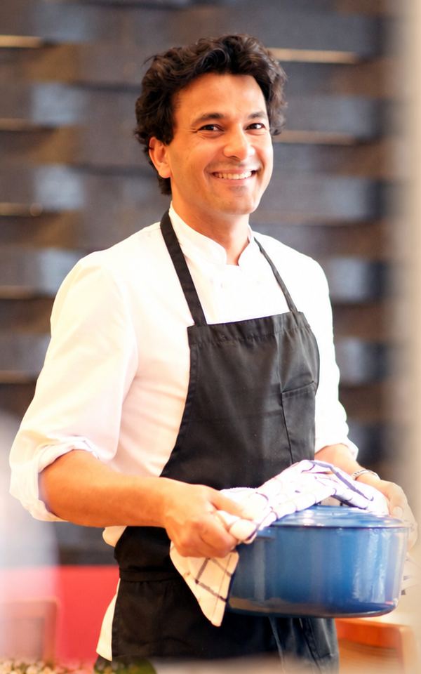 Chef Vikas Khanna smiling in his kitchen, holding a blue pot