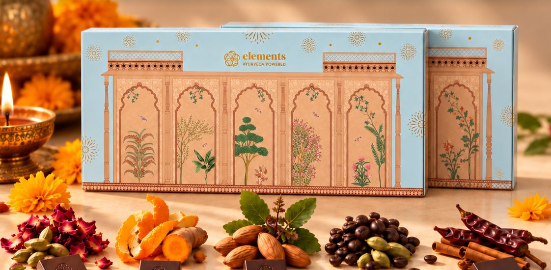 Two blue Ananda boxes side by side behind the five bars' spices, with a lit diya and marigolds